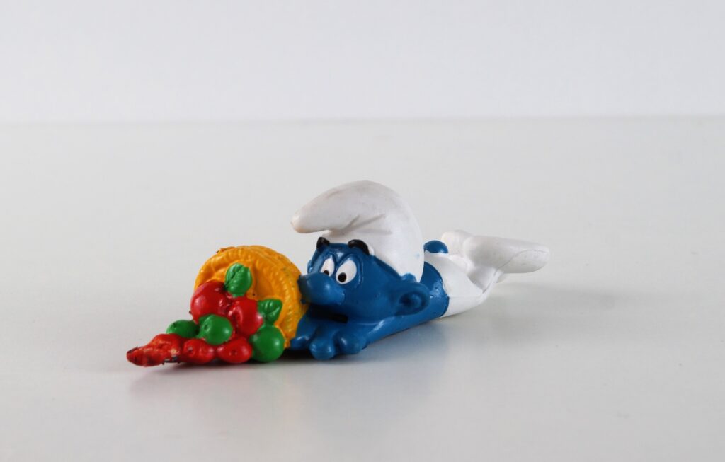 A smurf figurine lying down having fallen over and spilled a basket