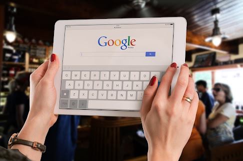Hands with red fingernails holding a tablet displaying the Google search bar